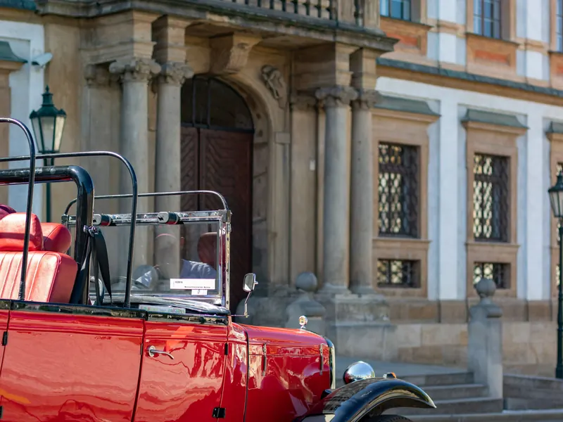Polished red vintage cabriolet parked in front of a baroque Prague palace